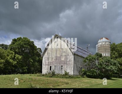 Une grande grange blanche et altérée se dresse avec un silo. Banque D'Images