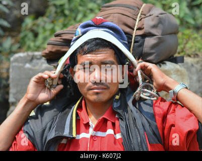 Le jeune téléporteur népalais (sherpa) à charge lourde prend une courte pause sur un banc de pierre et pose pour la caméra. Banque D'Images