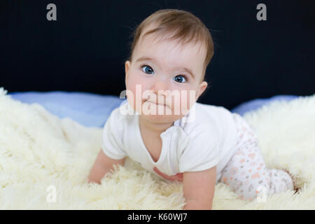 Beau petit bébé aux yeux bleus sur le lit. Banque D'Images