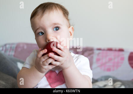 Petit enfant mange une pomme rouge à la maison libre. Banque D'Images