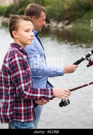 Teenage boy et père de pêche ensemble sur l'eau douce à partir de la rive du lac Banque D'Images