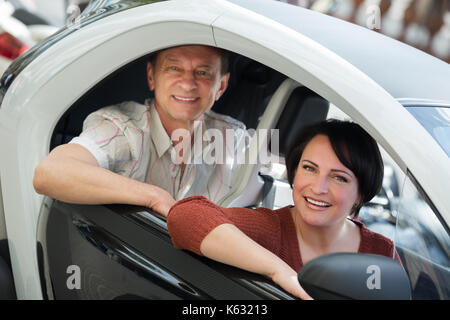 Portrait of smiling young man and woman standing près de l'extérieur électrique twizy Banque D'Images