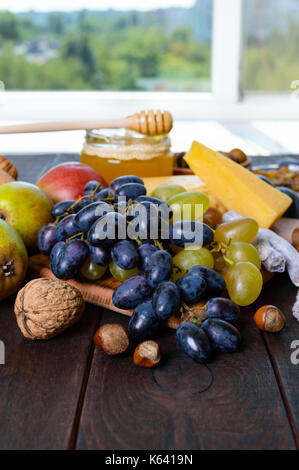 Un ensemble de produits : raisins, noix, miel, poires, fromage sur une table en bois foncé près de la fenêtre. Banque D'Images