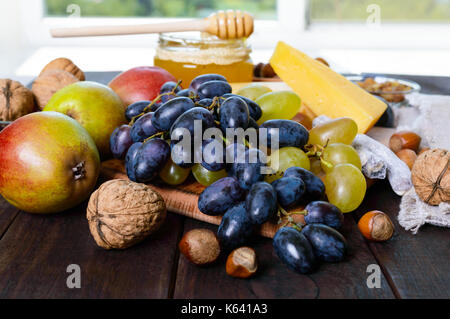 Un ensemble de produits : raisins, noix, miel, poires, fromage sur une table en bois foncé près de la fenêtre. Banque D'Images