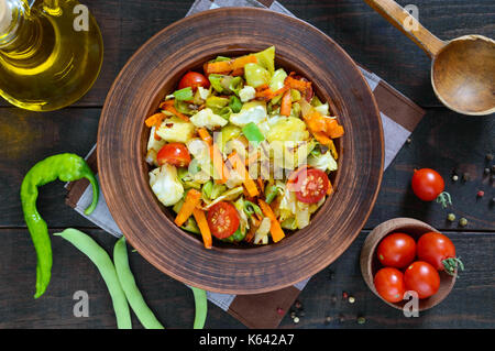 Ragoût aux légumes de choux, haricots verts, carottes, tomates, oignons, poivrons dans un bol d'argile sur un fond de bois foncé. salade végétarienne cu. Banque D'Images