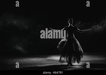 Silhouette élégante de lumière jeune ballerine debout dos à l'appareil photo en deuxième position des bras est sur le fond noir Banque D'Images