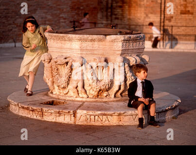 Venise, Vénétie, Italie. Enfants jouant autour de la tête de puits dans la région de Campo dei Frari Banque D'Images