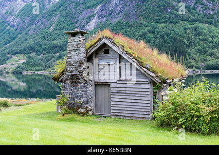 Studne vieille maison de bois avec la cheminée d'un toit en ardoise et empilé avec la plantation d'arbres et sur un fjord en Norvège avec jardin avec fleurs rouge un Banque D'Images