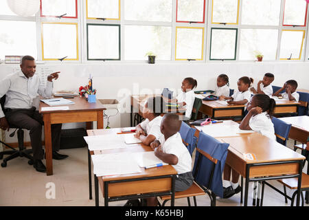 Enseignant d'enseigner aux enfants à partir de son bureau à l'école élémentaire Banque D'Images