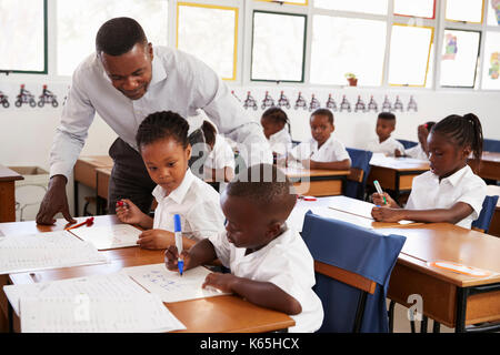 Professeur se tient à aider les enfants de l'école élémentaire à leur bureau Banque D'Images