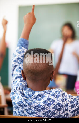 Vue arrière de boy raising hand à l'école élémentaire leçon Banque D'Images