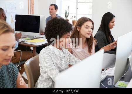 Deux femmes assis à un ordinateur discuter du travail en open plan office Banque D'Images