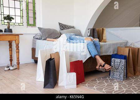 Femme de retour de voyage d'achats entouré de sacs se trouve sur lit Banque D'Images