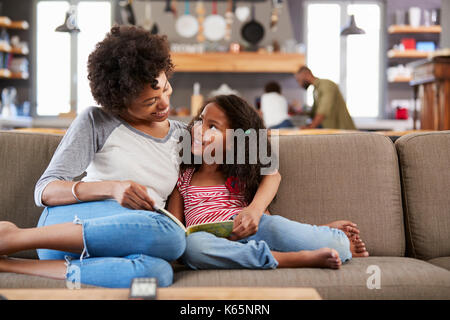 Mère et fille s'asseoir sur le canapé dans le salon lecture livre ensemble Banque D'Images