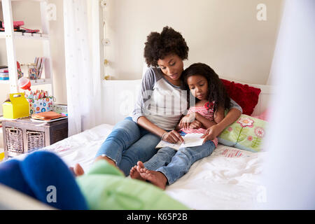 Mère et fille de l'emplacement On Bed Reading Book Together Banque D'Images