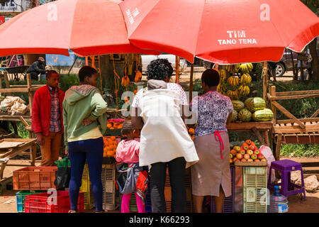 Les étals du marché à l'ombre sous les parasols vente de fruits et légumes en tant que peuple se parcourt, au Kenya Banque D'Images