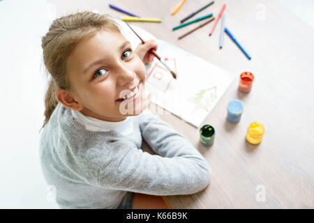 Happy smiling écolière est dessin. photo d'une mignonne petite fille fait ses devoirs. concept de l'éducation Banque D'Images