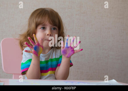 Portrait d'une petite fille aux palmiers peints. La fille est assise sur une chaise à la table Banque D'Images