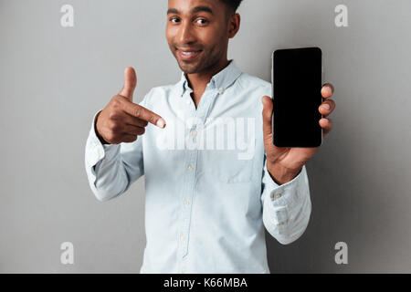 Joyeux excité homme africain face à l'écran vide isolé téléphone mobile sur fond gris Banque D'Images