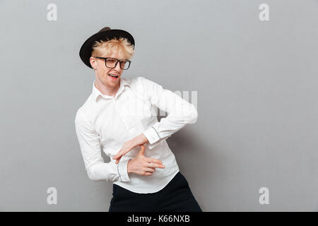 Image of happy young man wearing glasses isolés sur mur gris près de copyspace. À la caméra et s'amuser. Banque D'Images