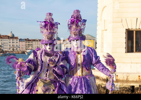 Carnaval de Venise 2017, Italie. Deux femmes en costumes colorés classique violet posant à San Giorgio Maggiore au coucher du soleil avec le phare et le lagon b Banque D'Images