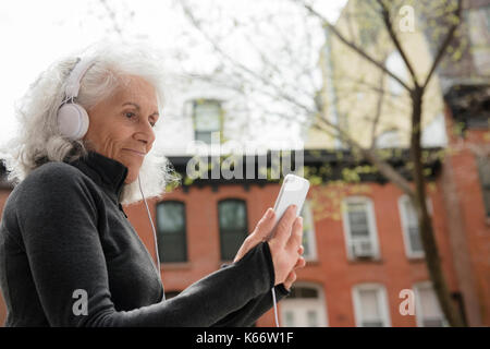 Femme plus l'écoute de téléphone cellulaire avec les écouteurs en ville Banque D'Images