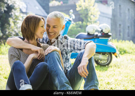 Couple assis dans l'herbe près de scooter Banque D'Images