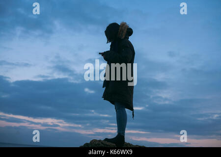 Caucasian woman wearing coat texting on cell phone at sunset Banque D'Images