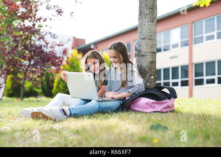 Deux élèves de sexe féminin souriant, assis sur l'herbe. Banque D'Images