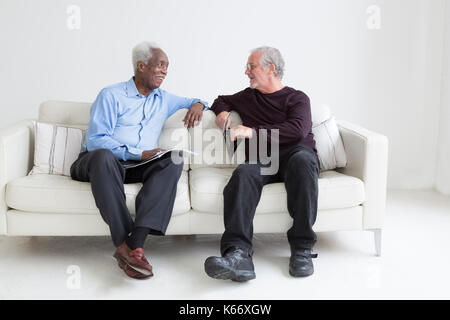 Les hommes plus âgés la lecture de revues sitting on sofa Banque D'Images