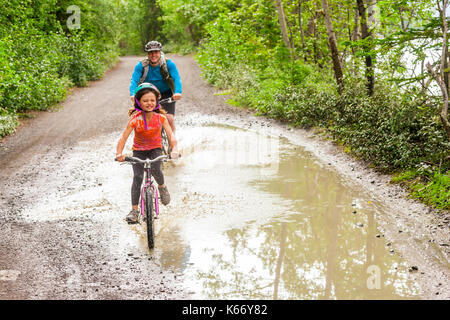 Père et fille la bicyclette par flaque Banque D'Images