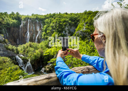 Older caucasian woman photographing cascades avec cell phone Banque D'Images