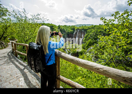 Older caucasian woman photographing cascades avec cell phone Banque D'Images