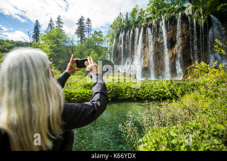 Older caucasian woman photographing waterfall with cell phone Banque D'Images