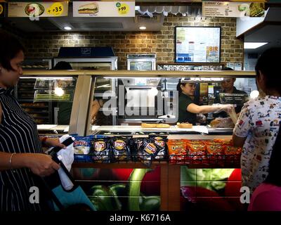 Pasig City, Philippines - septembre 8, 2017 : un client a l'air en tant que service crew prépare son sandwich dans un restaurant fast-food. Banque D'Images