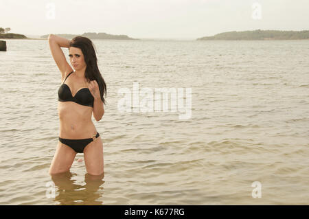 Jolie fille aux cheveux noirs portant un bikini noir par la mer Banque D'Images