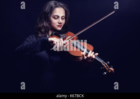 Jeune femme jouant du violon sur un fond sombre. Studio photo Banque D'Images