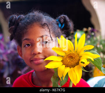 Jeune fille sourit joyeusement tout en maintenant un tournesol à la main qui a grandi Banque D'Images