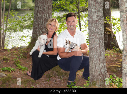 Portrait d'une femme blonde avec des ancêtres autochtones et un homme aux cheveux noirs, assis dans les bois avec leurs chiens de compagnie Banque D'Images