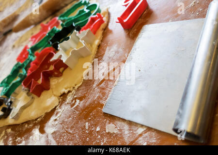 Emporte-pièces de Noël en pâte à sucre coincé sur une table fleurie avec un racloir de pâte à côté. Banque D'Images