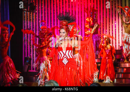 Singer en robe rouge et danseuses exotiques en live sur scène dans des costumes colorés dans un cabaret show pour les touristes dans une boîte de nuit à La Havane, Cuba Banque D'Images