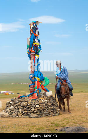 Oulan-bator, Mongolie - 12 juin 2007 : un homme en vêtements traditionnels mongols riding horse, circumambulating autour de petits stupa et les drapeaux de prières sur th Banque D'Images