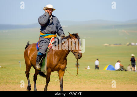 Oulan-bator, Mongolie - 12 juin 2007 : un homme à cheval mongol traditionnel parlant dans un téléphone portable moderne tout en montant sur l'herbe de la steppe Banque D'Images