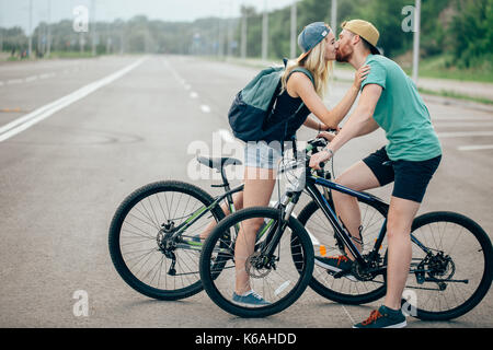 Beau jeune couple dans l'amour de marcher avec des bicyclettes, embrasser et s'étreindre. Se tenir près de la bicyclette. La notion de repos actif Banque D'Images