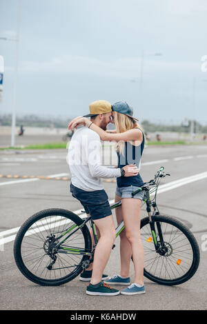 Beau jeune couple dans l'amour de marcher avec des bicyclettes, embrasser et s'étreindre. Se tenir près de la bicyclette. La notion de repos actif Banque D'Images