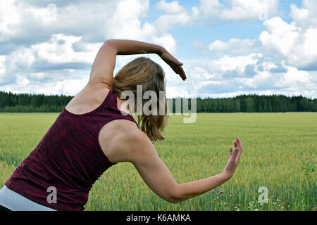Middle aged woman stretching yoga et l'exercice à l'extérieur. Vue arrière, champ sur l'arrière-plan. Banque D'Images