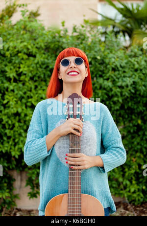 Femme aux cheveux rouges avec une guitare dans un parc bénéficiant d'avec la musique Banque D'Images