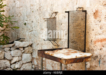 Old rusty barbecue pendu sur la maison de pierre sur l'île méditerranéenne Banque D'Images