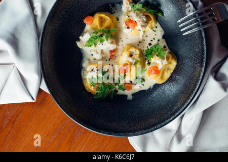 Vue rapprochée de la viande bouillie dumpling faits maison servis dans la plaque d'argile quenelles avec sauce crémeuse et cuillère en bois. composition dans un style rustique en bois sur Banque D'Images