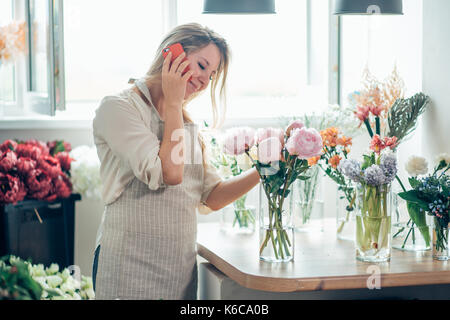 Portrait of young female florist parlant au téléphone et prendre des notes à un fleuriste. Banque D'Images